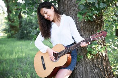 ormanda yürüyüş ve iskambil gitar, yaz doğa, parlak güneş ışığı, gölgeler ve yeşil yaprakları, romantik duygular genç kadın