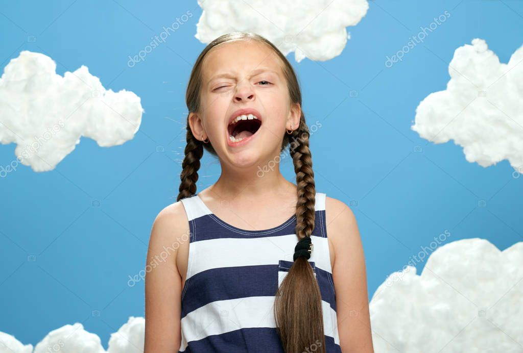 girl dressed in striped dress posing on a blue background with cotton clouds, the concept of summer and happiness