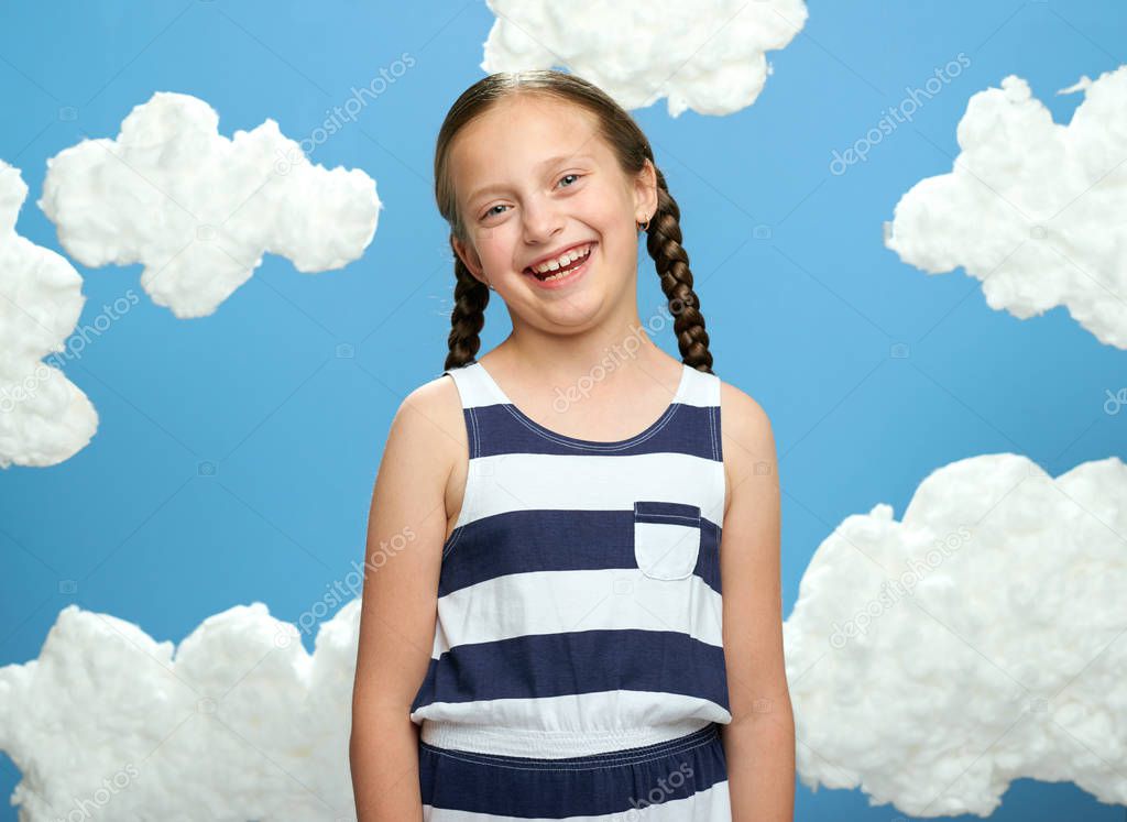 girl dressed in striped dress posing on a blue background with cotton clouds, the concept of summer and happiness