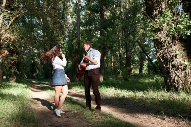 Genç çift, ormanda yürüyüş gitar çalmak ve dans, yaz doğa, parlak güneş ışığı, gölgeler ve yeşil yaprakları, romantik duygular