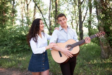 Genç çift, ormanda yürüyüş gitar çalmak ve dans, yaz doğa, parlak güneş ışığı, gölgeler ve yeşil yaprakları, romantik duygular