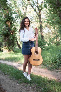 ormanda yürüyüş ve iskambil gitar, yaz doğa, parlak güneş ışığı, gölgeler ve yeşil yaprakları, romantik duygular genç kadın