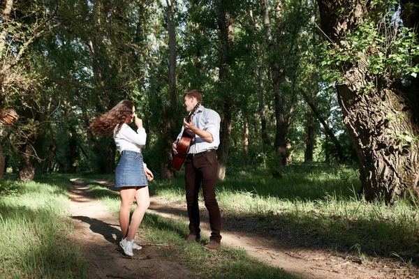 Genç çift, ormanda yürüyüş gitar çalmak ve dans, yaz doğa, parlak güneş ışığı, gölgeler ve yeşil yaprakları, romantik duygular