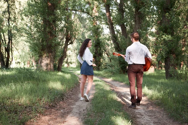 Genç çift, ormanda yürüyüş gitar çalmak ve dans, yaz doğa, parlak güneş ışığı, gölgeler ve yeşil yaprakları, romantik duygular