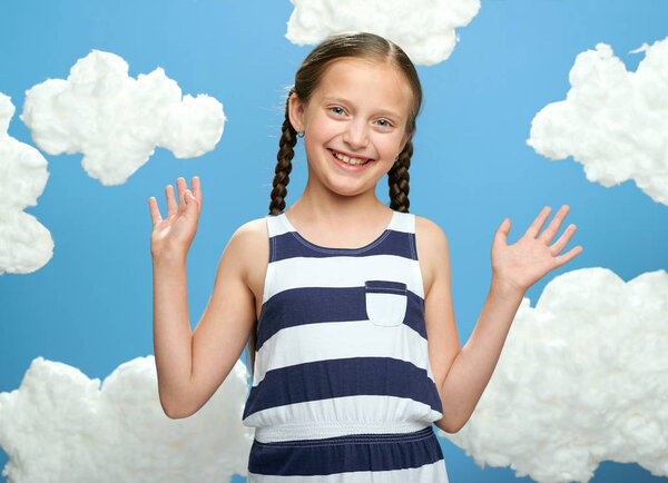 girl dressed in striped dress posing on a blue background with cotton clouds, the concept of summer and happiness