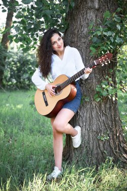 ormanda yürüyüş ve iskambil gitar, yaz doğa, parlak güneş ışığı, gölgeler ve yeşil yaprakları, romantik duygular genç kadın