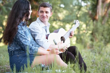 Genç çift ormanda oturan ve iskambil gitar, yaz doğa, parlak güneş ışığı, gölgeler ve yeşil yaprakları, romantik duygular