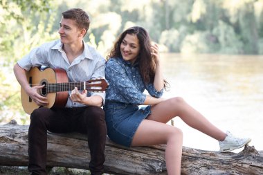 Genç çift, bir günlük nehrin yanında oturan ve iskambil gitar, yaz doğa, parlak güneş ışığı gölgeler ve yeşil yaprakları, romantik duygular