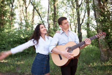 Genç çift, ormanda yürüyüş gitar çalmak ve dans, yaz doğa, parlak güneş ışığı, gölgeler ve yeşil yaprakları, romantik duygular