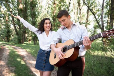 Genç çift, ormanda yürüyüş gitar çalmak ve dans, yaz doğa, parlak güneş ışığı, gölgeler ve yeşil yaprakları, romantik duygular