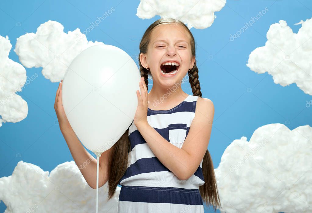 girl dressed in striped dress posing on a blue background with cotton clouds, the concept of summer and happiness