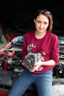 kırık bir araba ve kötü bir bölümü, bir elektrik jeneratörü nasıl tamir için anlamak değil yedek tutar genç bir kız duruyor