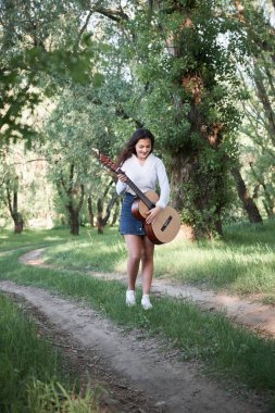 ormanda yürüyüş ve iskambil gitar, yaz doğa, parlak güneş ışığı, gölgeler ve yeşil yaprakları, romantik duygular genç kadın
