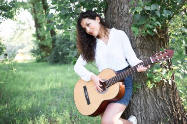 ormanda yürüyüş ve iskambil gitar, yaz doğa, parlak güneş ışığı, gölgeler ve yeşil yaprakları, romantik duygular genç kadın