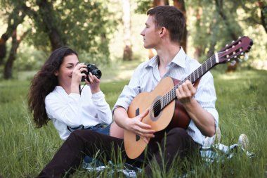 ormanda oturan ve fotoğrafta eski fotoğraf makinesi, yaz doğa, parlak güneş ışığı, gitar, çalmak genç çift gölgeler ve yeşil yaprakları, romantik duygular