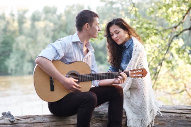 Genç çift, bir günlük nehrin yanında oturan ve iskambil gitar, yaz doğa, parlak güneş ışığı gölgeler ve yeşil yaprakları, romantik duygular