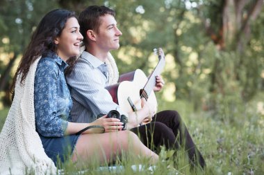 Genç çift ormanda oturan ve iskambil gitar, yaz doğa, parlak güneş ışığı, gölgeler ve yeşil yaprakları, romantik duygular