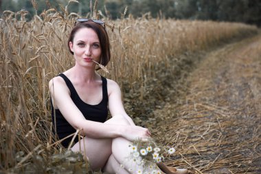 çıplak ayakla buğday alan, yaz ve seyahat kavramı yakınındaki toprak yolda oturan genç kız