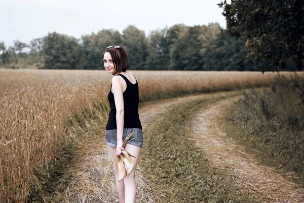 年轻女孩赤脚走在地上的路穿过田野和森林 夏天和旅行的概念 — 图库照片
