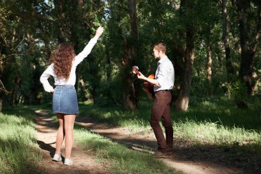 Genç çift, ormanda yürüyüş gitar çalmak ve dans, yaz doğa, parlak güneş ışığı, gölgeler ve yeşil yaprakları, romantik duygular