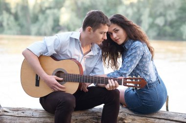 Genç çift, bir günlük nehrin yanında oturan ve iskambil gitar, yaz doğa, parlak güneş ışığı gölgeler ve yeşil yaprakları, romantik duygular