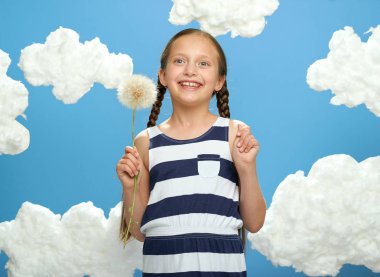 kız büyük bir karahindiba çizgili elbise giymiş elleri pamuk bulutlar, yaz, tatil ve mutluluk kavramı ile mavi bir arka plan üzerinde poz vardır