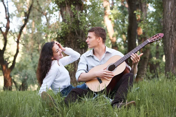 Genç çift ormanda oturan ve iskambil gitar, yaz doğa, parlak güneş ışığı, gölgeler ve yeşil yaprakları, romantik duygular