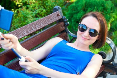 dinlenme veya bir selfie alarak şehir sokak, bir bankta yalan uzun mavi elbiseli kız