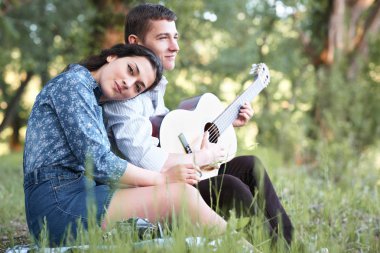 Genç çift ormanda oturan ve iskambil gitar, yaz doğa, parlak güneş ışığı, gölgeler ve yeşil yaprakları, romantik duygular