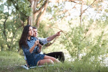 Genç çift, ormandaki çimlerde oturan fotoğraf çekmek ve seyir günbatımı, yaz doğa, parlak güneş ışığı, gölgeler ve yeşil yaprakları, romantik duygular