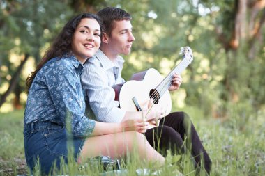 Genç çift ormanda oturan ve iskambil gitar, yaz doğa, parlak güneş ışığı, gölgeler ve yeşil yaprakları, romantik duygular