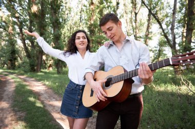 Genç çift, ormanda yürüyüş gitar çalmak ve dans, yaz doğa, parlak güneş ışığı, gölgeler ve yeşil yaprakları, romantik duygular
