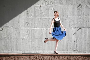 Genç kız bir beton duvara poz giyinmiş siyah, sert ışık ve gölge