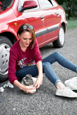 kırık bir arabanın yakınında oturan ve onu orada yanında yardım arayan bir genç kızsın kötü parçalar, elektrik jeneratörü, araçları ve ilk yardım kiti