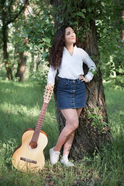 ormanda yürüyüş ve iskambil gitar, yaz doğa, parlak güneş ışığı, gölgeler ve yeşil yaprakları, romantik duygular genç kadın