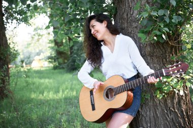 ormanda yürüyüş ve iskambil gitar, yaz doğa, parlak güneş ışığı, gölgeler ve yeşil yaprakları, romantik duygular genç kadın