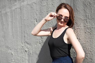 Genç kız bir beton duvara poz giyinmiş siyah, sert ışık ve gölge