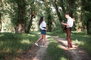 Genç çift, ormanda yürüyüş gitar çalmak ve dans, yaz doğa, parlak güneş ışığı, gölgeler ve yeşil yaprakları, romantik duygular