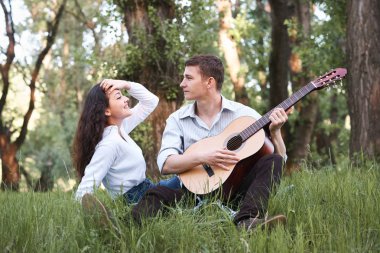 Genç çift ormanda oturan ve iskambil gitar, yaz doğa, parlak güneş ışığı, gölgeler ve yeşil yaprakları, romantik duygular