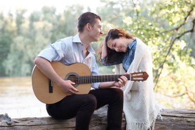 Genç çift, bir günlük nehrin yanında oturan ve iskambil gitar, yaz doğa, parlak güneş ışığı gölgeler ve yeşil yaprakları, romantik duygular