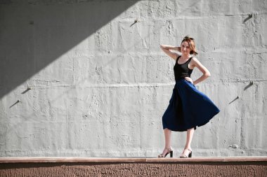 Genç kız bir beton duvara poz giyinmiş siyah, sert ışık ve gölge