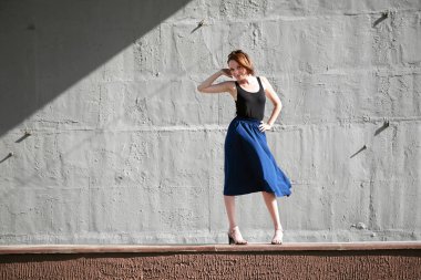 Genç kız bir beton duvara poz giyinmiş siyah, sert ışık ve gölge