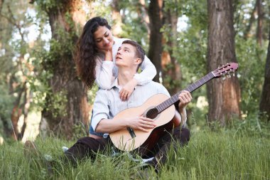 Genç çift ormanda oturan ve iskambil gitar, yaz doğa, parlak güneş ışığı, gölgeler ve yeşil yaprakları, romantik duygular