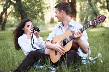 ormanda oturan ve fotoğrafta eski fotoğraf makinesi, yaz doğa, parlak güneş ışığı, gitar, çalmak genç çift gölgeler ve yeşil yaprakları, romantik duygular