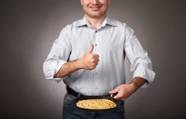 man posing with a pancake in a pan, white shirt and pants, gray background, shallow depth of field, sharp pancake and blurred face