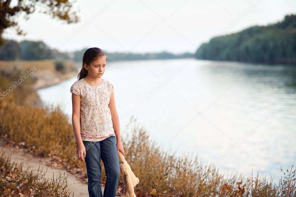 the girl child with toy bear walking along the path in the forest at sunset, beautiful river and landscape