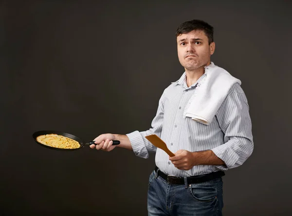 man posing with a pancake in a pan, white shirt and pants, gray background, surprised emotions