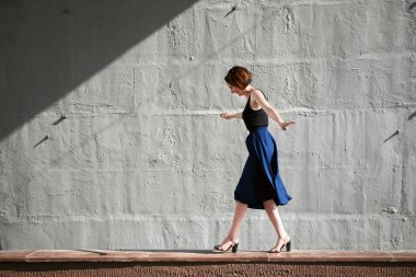 Genç kız bir beton duvara poz giyinmiş siyah, sert ışık ve gölge