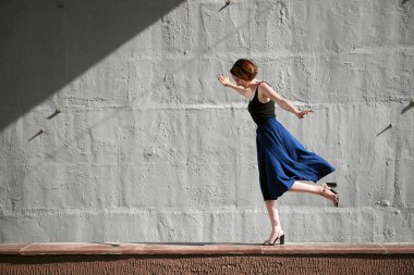 Genç kız bir beton duvara poz giyinmiş siyah, sert ışık ve gölge