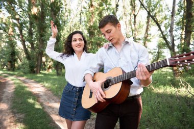 Genç çift, ormanda yürüyüş gitar çalmak ve dans, yaz doğa, parlak güneş ışığı, gölgeler ve yeşil yaprakları, romantik duygular